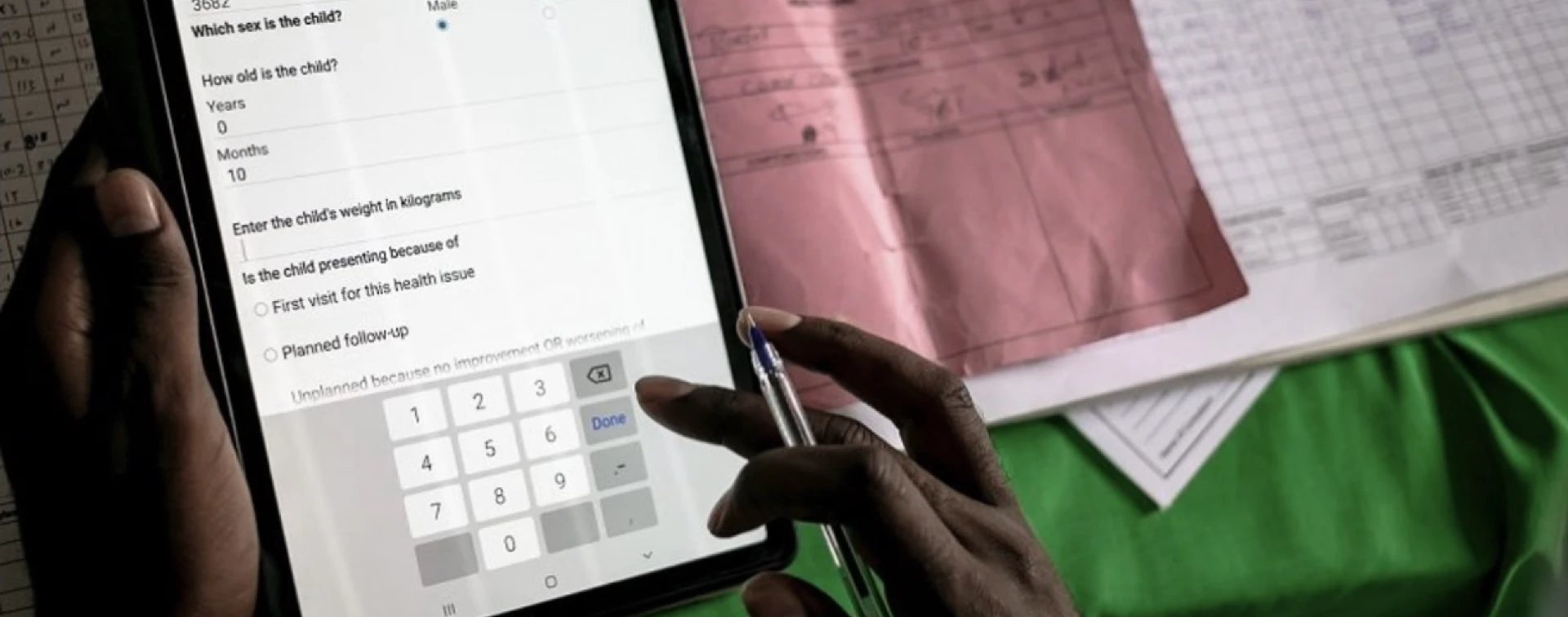 Health worker entering child patient data on a tablet during a clinic visit